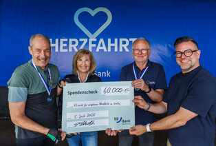 Eine Gruppe von vier Personen hält einen großen Scheck über 60.000 Euro vor einem blauen Hintergrund mit dem Schriftzug "HERZFAGHRT". Der Scheck ist für die Klinik für angewandte Herzmedizin. Alle Personen tragen Medaillen und strahlen Freude aus.