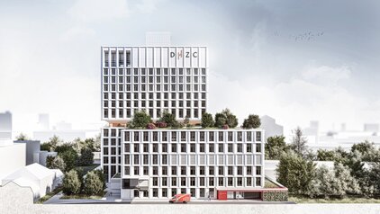 Das Bild zeigt ein modernes, mehrstöckiges Gebäude mit einer glatten, weißen Fassade. Oben sind begrünte Terrassen sichtbar, während im Vordergrund ein rotes Notarztfahrzeug steht. Um das Gebäude sind Bäume und Sträucher angeordnet, was eine einladende Umgebung schafft.