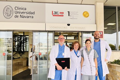 Das Bild zeigt vier medizinische Fachkräfte vor dem Eingang der Clínica Universidad de Navarra. Sie tragen weiße Kittel und lächeln freundlich in die Kamera. Im Hintergrund ist ein Schild mit dem Kliniknamen und dem Hinweis auf externe Konsultationen sichtbar.