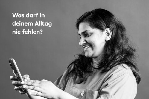 Das Foto der Serie "Sag jetzt nichts" zeigt die Pflegekraft Merin Rajan aus Indien mit der Frage "Was darf in deinem Alltag nicht fehlen?", die ein Handy in der Hand hält.