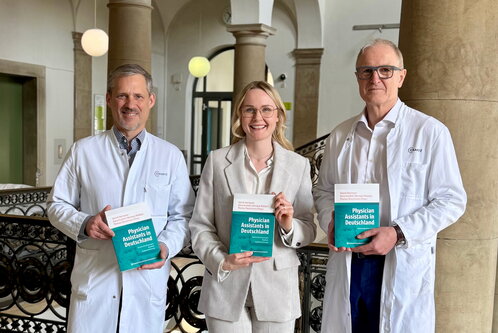 Prof. Christoph Starck, Daria Hunfeld und Prof. Volkmar Falk (von links nach rechts) stehen im Treppenhaus des Deutschen Herzzentrums der Charité und präsentieren das frisch erschienene Fachbuch „Physician Assistants in Deutschland“.