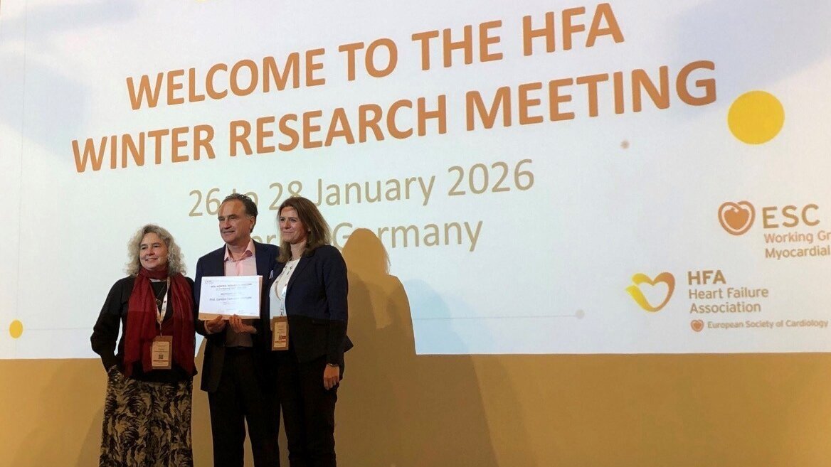 Drei Personen stehen auf einer Bühne vor einem Banner mit dem Titel „Willkommen zum HFA Winter Research Meeting“ und den Daten 26. bis 28. Januar 2026 in Deutschland. Zwei der Personen halten eine Auszeichnung oder ein Dokument in den Händen.