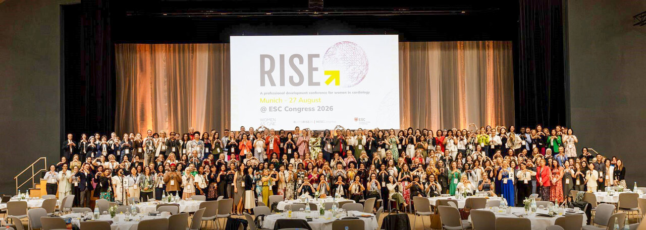 Gruppennahaufnahme von Teilnehmerinnen und Teilnehmern eines Kongresses, die vor einer großen Leinwand mit der Aufschrift "RISE" stehen. Der Raum ist festlich dekoriert, und die Anwesenden tragen verschiedene formelle Kleidung. Es handelt sich um eine Veranstaltung im Jahr 2023.