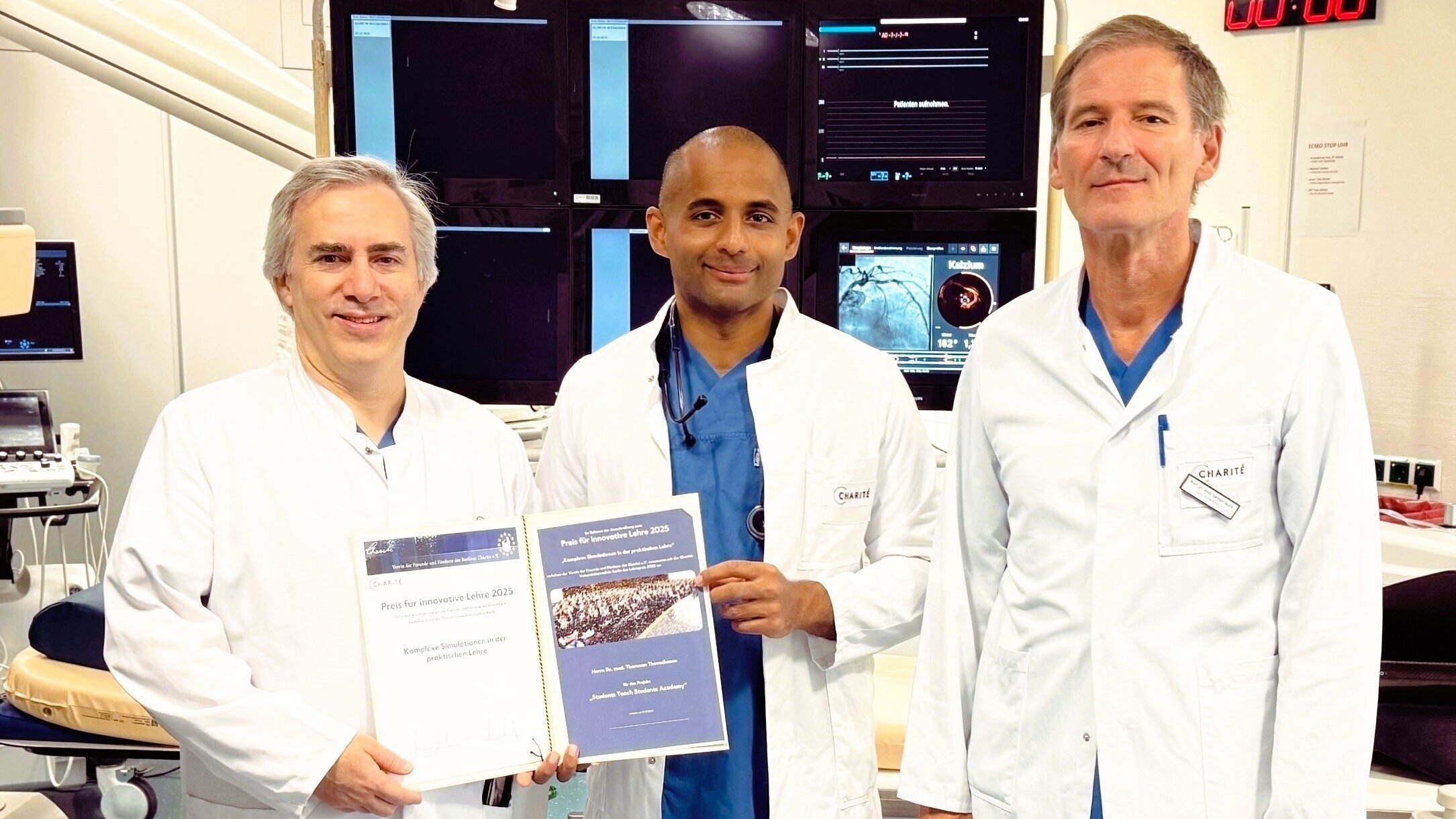 Drei Ärzte in weißen Kitteln stehen in einem modernen Krankenhausraum. Sie halten Zertifikate für den Preis für innovative Lehre 2025. Im Hintergrund sind medizinische Geräte und Bildschirme sichtbar. Alle drei lächeln stolz in die Kamera.