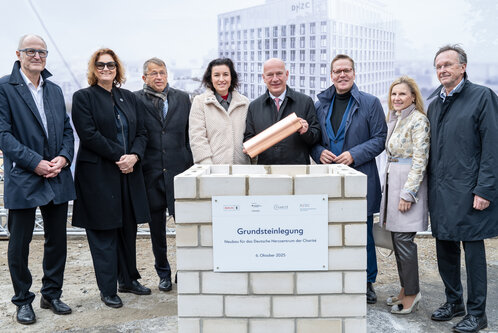 Die Grundsteinlegung für den Neubau des Deutschen Herz-Zentrums der Charité fand am 6. Oktober 2025 statt. Mehrere Personen stehen um einen Mauerstein mit einer Tafel, die Informationen zum Projekt enthält. Einer der Anwesenden hält eine Kupferkapsel.